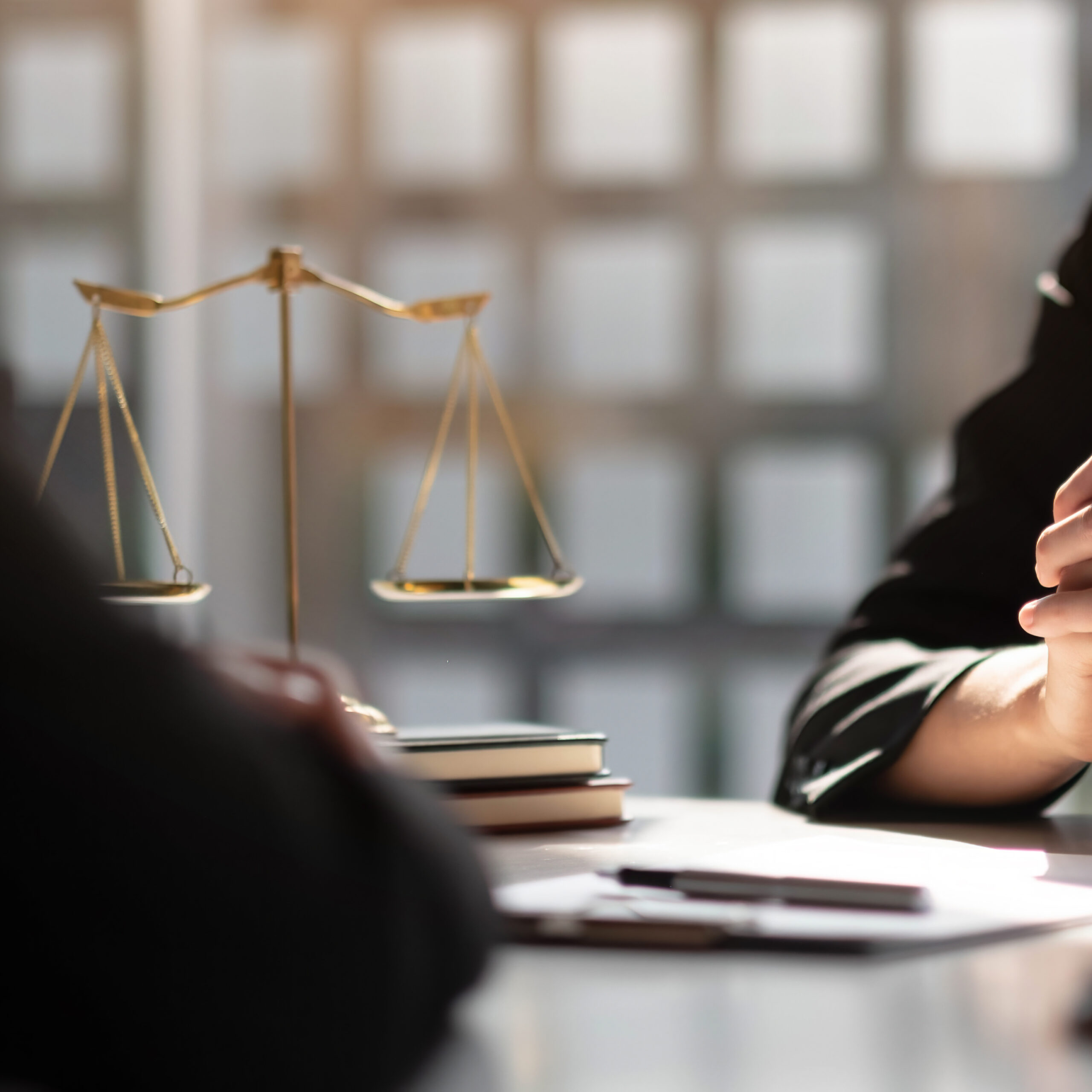 scales of justice on desk with a client and lawyer sitting across from each other