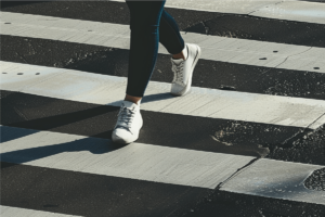 a woman walking across a crosswalk in white sneakers